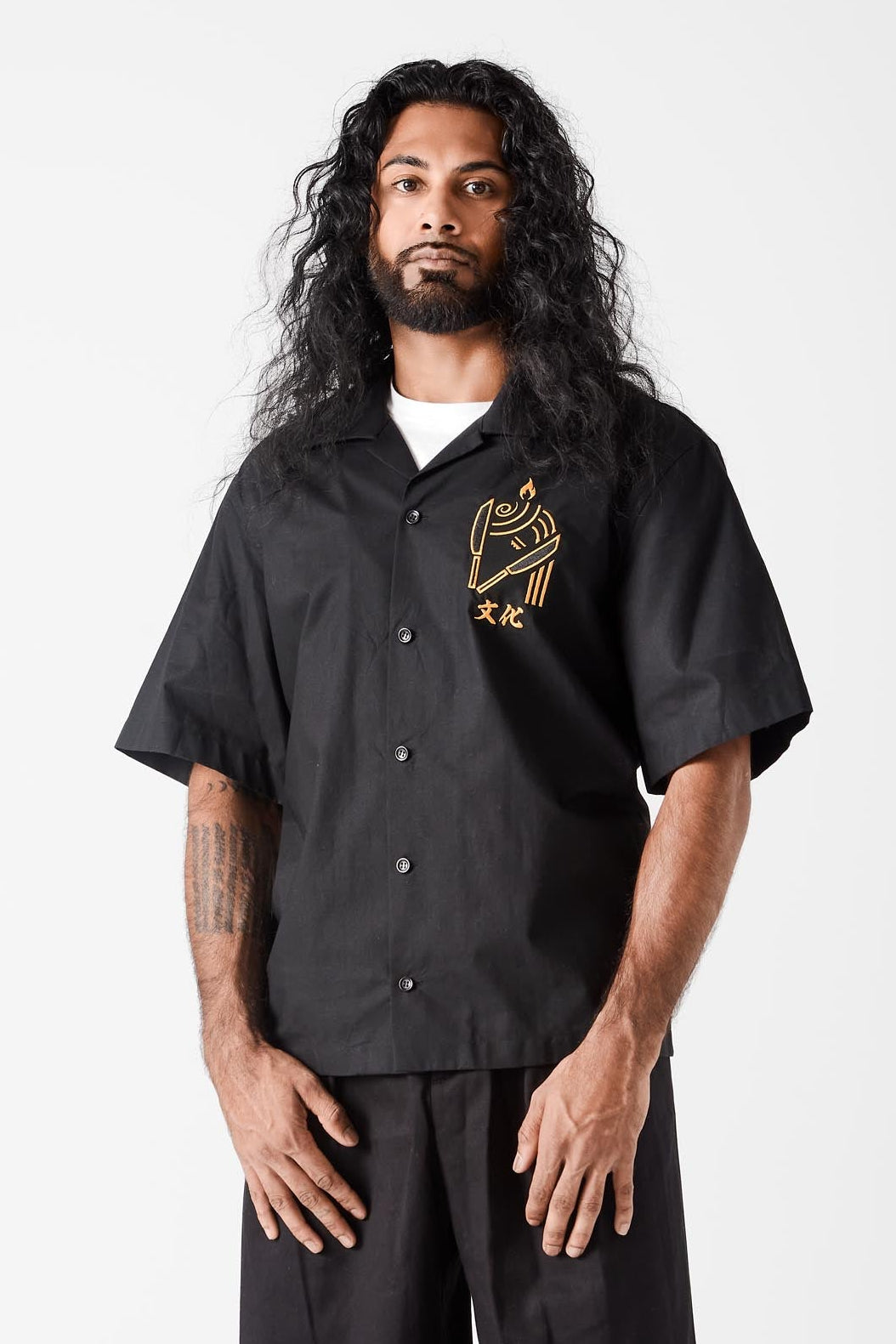 Man wearing a black shirt with a logo and black pants on a white background